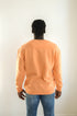 Person wearing an orange long-sleeve shirt and blue jeans against a white background