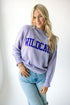 A woman wearing a purple turtleneck sweater with the word 'WILDCATS' across the front in blue letters, paired with blue jeans.