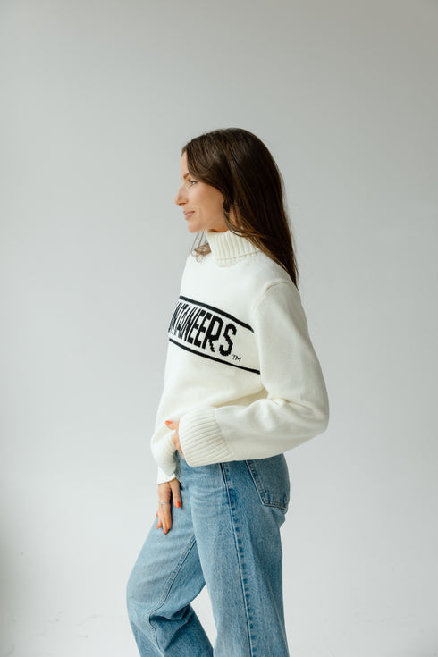Woman wearing a white sweater with text and blue jeans on a plain background