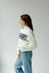 Woman wearing a white sweater with text and blue jeans on a plain background