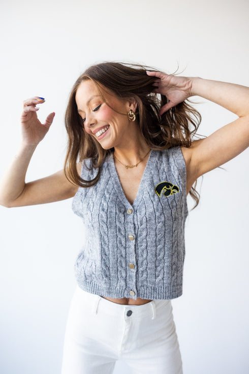 Woman wearing a gray cable knit vest with a logo on a white background
