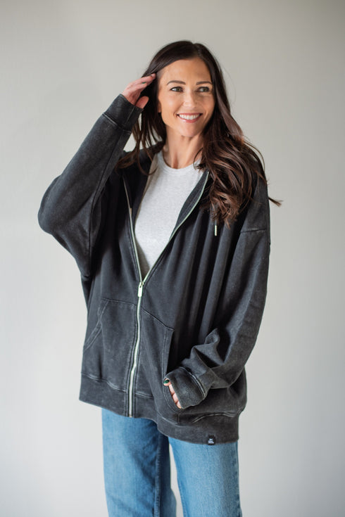 Woman wearing a dark gray zip-up hoodie and blue jeans against a plain background