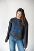 Woman wearing a dark gray sweatshirt with blue text and jeans on a white background
