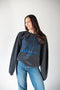 Woman wearing a dark gray sweatshirt with blue text and jeans on a white background
