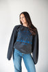 Woman wearing a dark gray sweatshirt with blue text and jeans on a white background